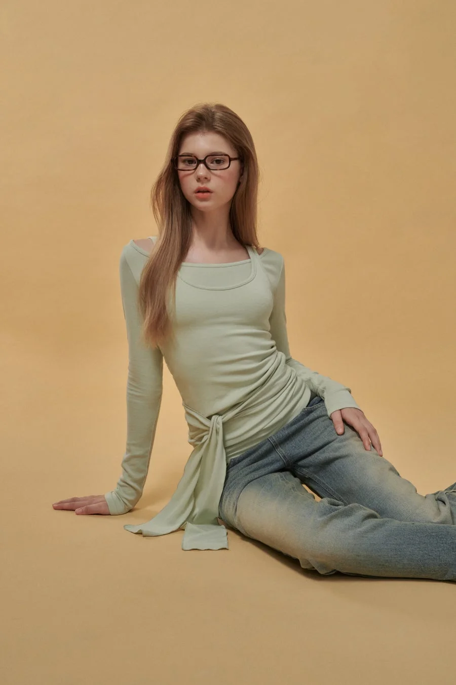 淡いグリーンのトップスとデニムを着用した女性モデル
