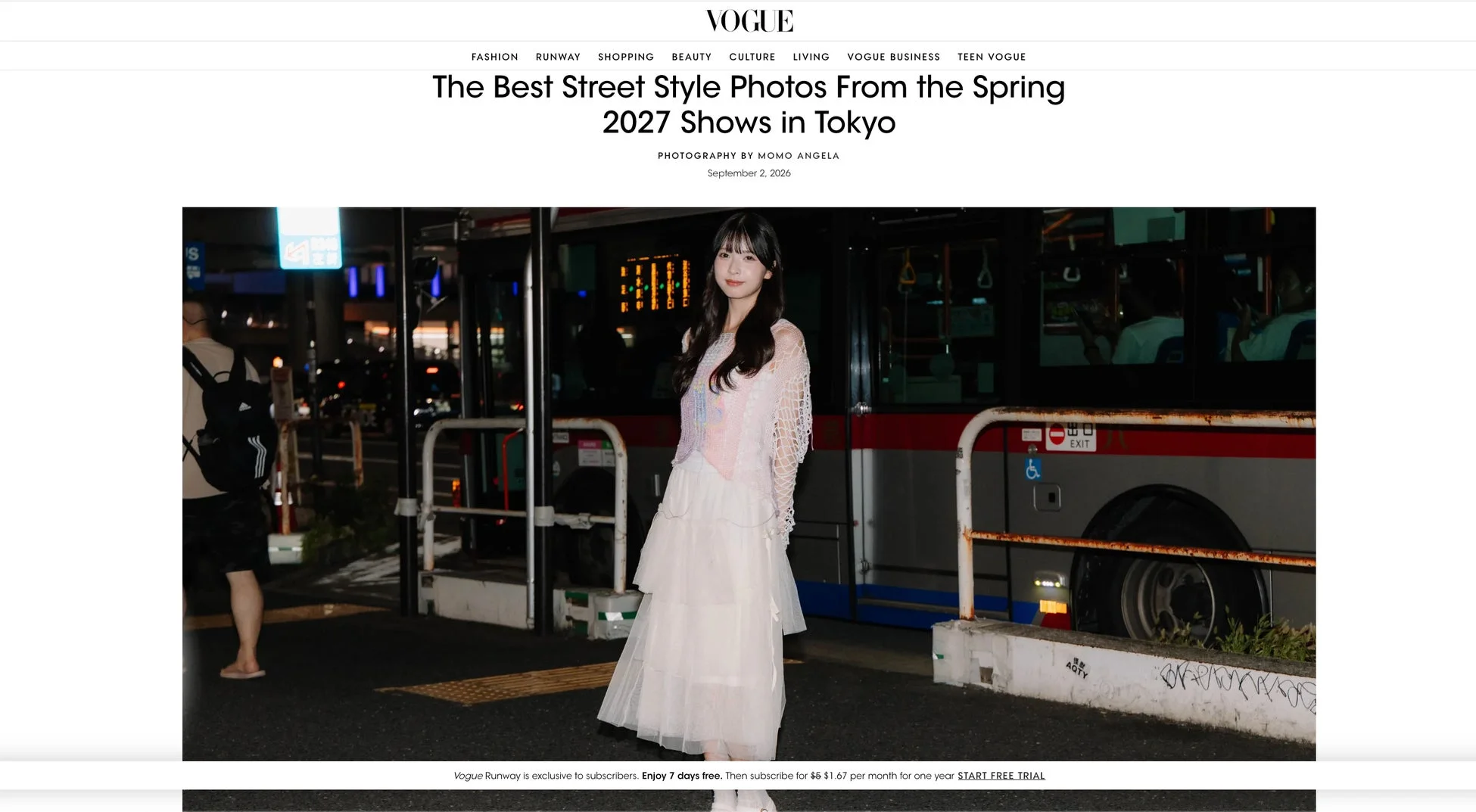 VOGUEの記事ページに掲載された、東京の夜のストリートスナップ。白いドレスとクロシェニットを着用した若い女性が、バスを背景に街角でポーズをとっている写真です。