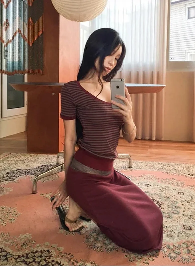 ストライプのトップスとワインレッドのロングスカートを着用し自撮りする女性