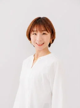 白い背景の前で、笑顔でカメラを見つめるショートヘアの女性のポートレート
