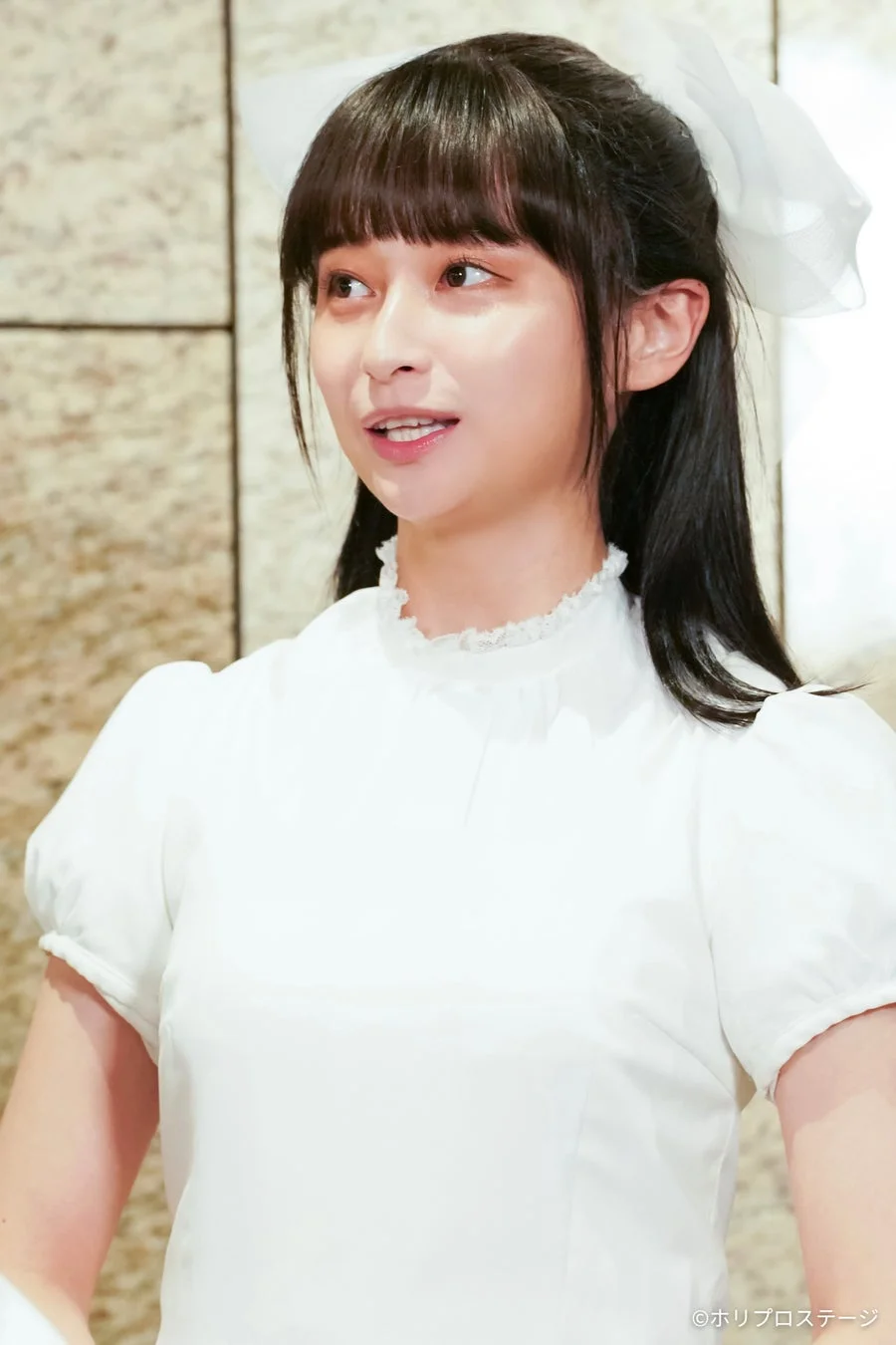 白いブラウスと大きな白いリボンを身につけた若い女性のポートレートです。彼女は笑顔で、少し左を向いています。