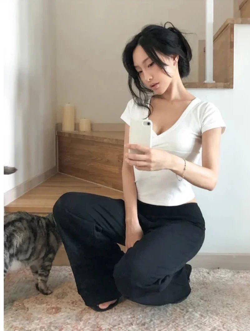 白いTシャツと黒いパンツ姿で自撮りをする女性と猫