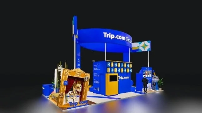 Trip.com Groupの青と黄色のモダンな展示ブースが写っています。ブースには「CIAO VENEZIA」と書かれた金色の額縁の中にベネチア風の仮面が飾られています