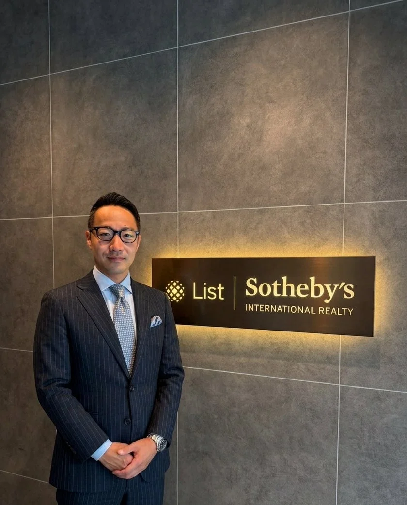 スーツを着たビジネスマンが、List Sotheby's INTERNATIONAL REALTYのロゴが光る壁の前で立っている