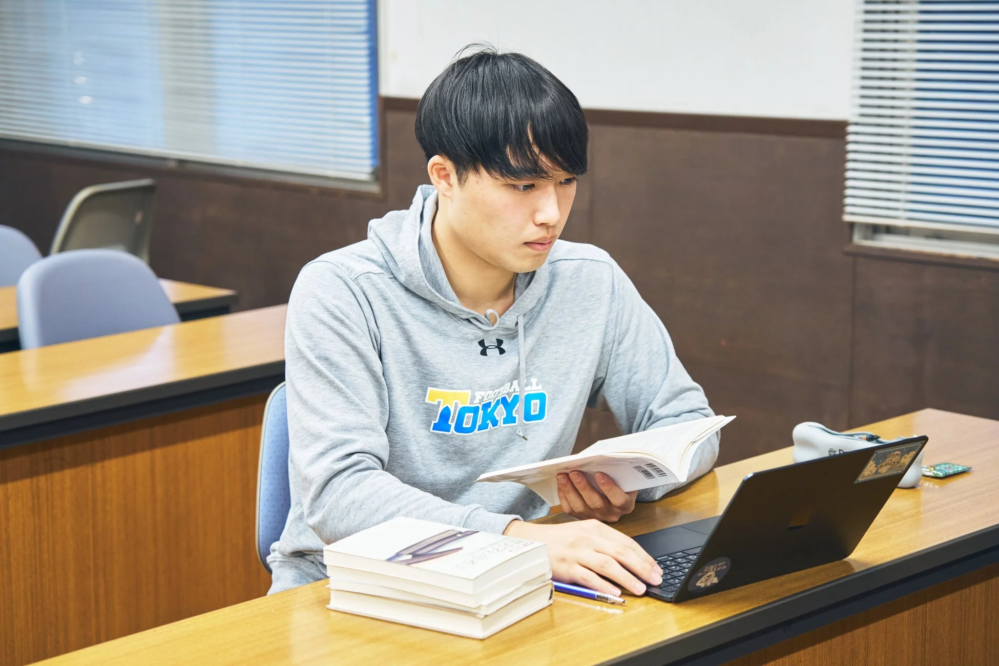 教室でノートパソコンと本を使って勉強する若い男性