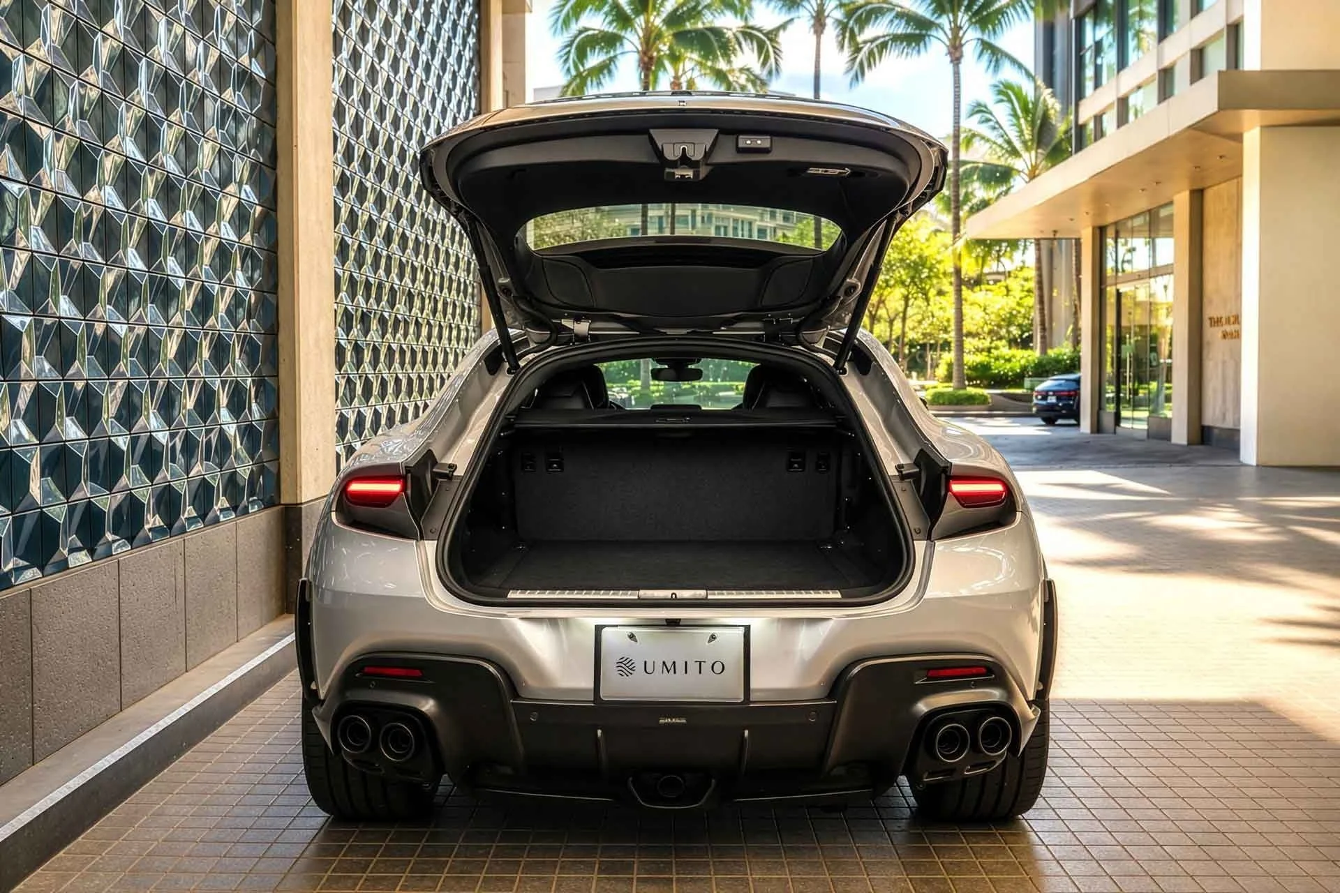 シルバーの高級車がトランクを開けて駐車している様子です。背景にはヤシの木とモダンな建物が見え、リゾートのような雰囲気があります。