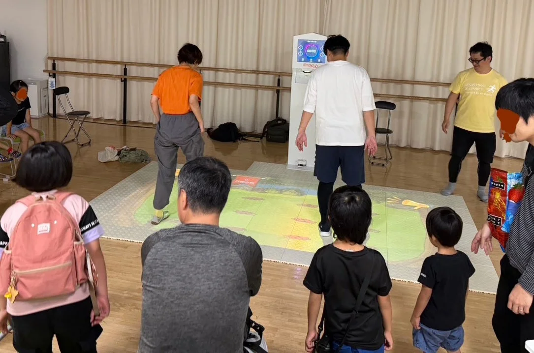 室内で大人と子供たちがインタラクティブなフロアプロジェクションゲームに参加している様子