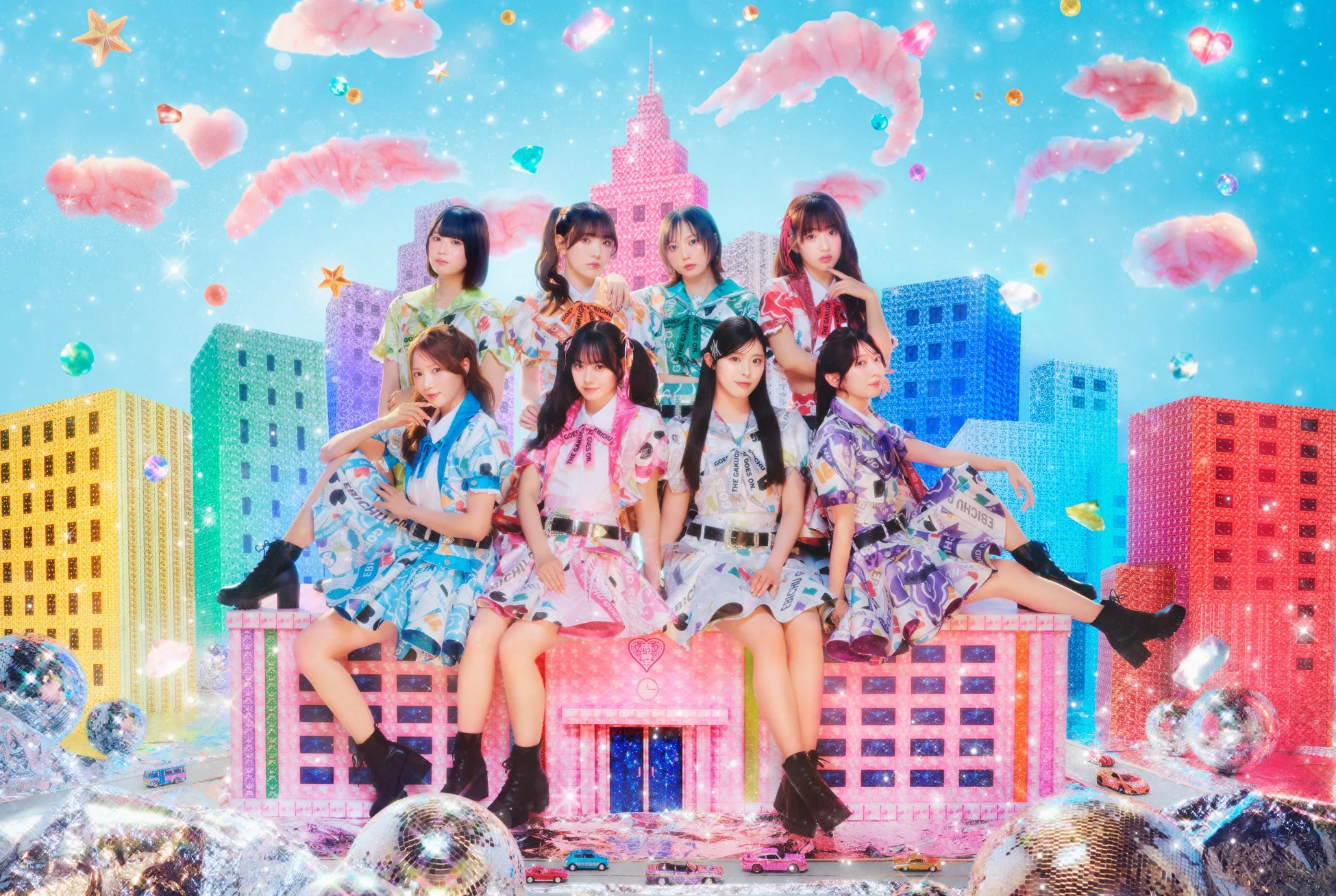 8人組の女性アイドルグループがファンタジーな都市を背景にポーズ