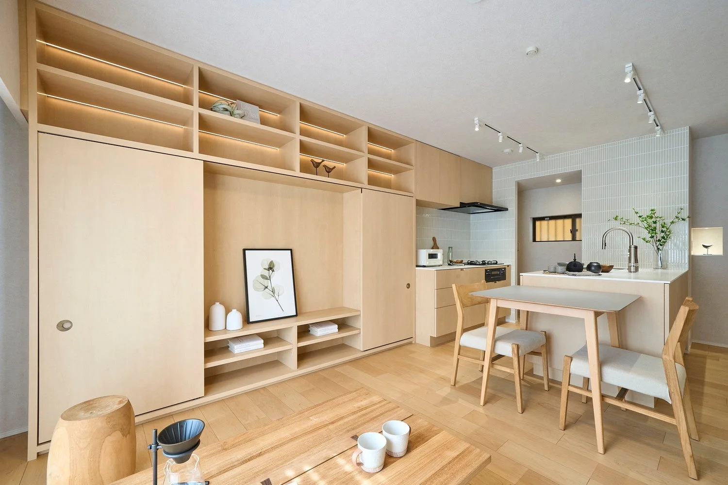 明るい木材を基調としたモダンなLDK空間です。オープンシェルフの間接照明が特徴で、アイランドキッチンとダイニングテーブルが配置された、機能的かつナチュラルなインテリアです。
