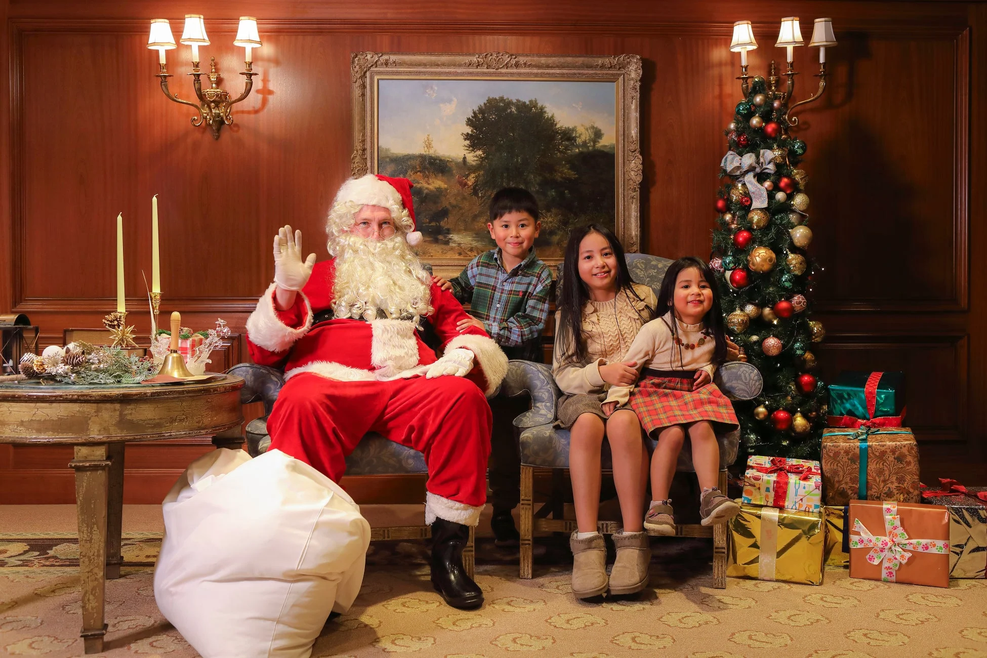 サンタクロースが3人の子供たちと一緒にクリスマスツリーやプレゼントに囲まれた部屋で記念撮影をしている様子です。